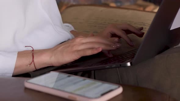 Close Up Of Women's Hands Typing On A Laptop Keyboard Next To A Smartphone