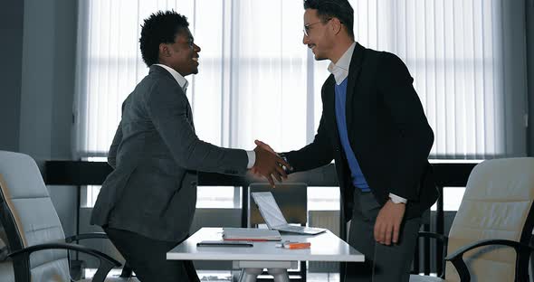 Two Young Businessman Talking at Desk in Office