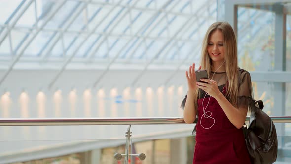 Happy Teenage Girl Holding Bags with Purchases, Smiling While Looking at Phone in Shopping Center