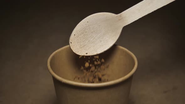 Coffee Falls From a Wooden Spoon Into a Paper Craft Glass on a Gray Background