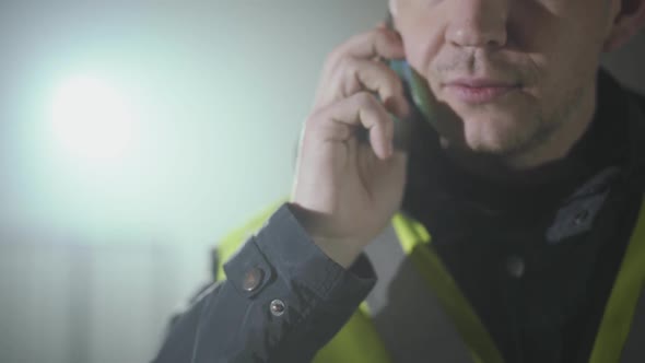 Close Up Portrait of the Man in the Builders Uniform and Helmet Talking By Cell Phone in Front of