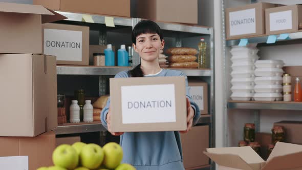 Portrait of Caucasian Woman Holding Cardboard Donation Box with Grocery While Standing at Charitable