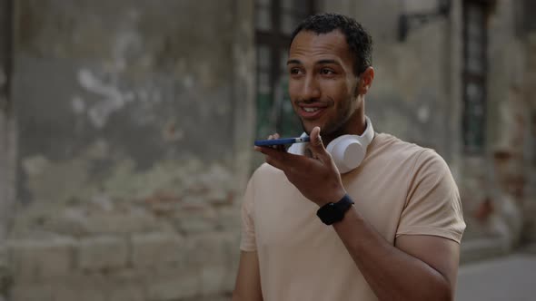 Side View of the African American Runner Walks Down the Street and Records a Voice Message Wearing