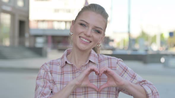Loving Young Woman Showing Heart Shape By Hands Outdoor