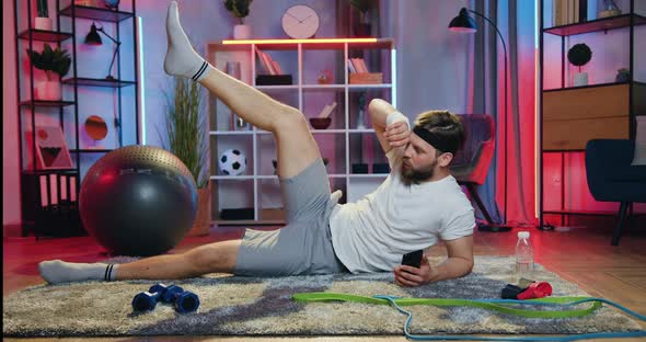 Man in Sportswear Lying on the Floor in the Evening and Doing Leg lifts Exercises