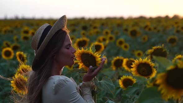 Young Woman with Long Hair and Straw Hat in a Beautiful Field of Sunflowers at Sunset Time