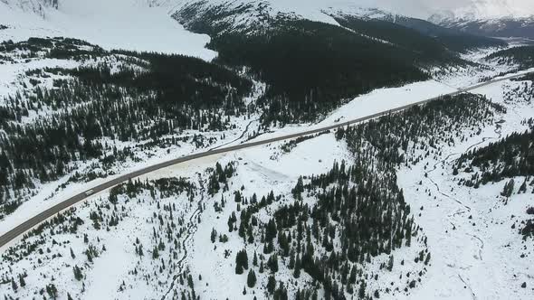 White car drives along the road in the black forest through snowy rocky mountains in Alberta, Canada