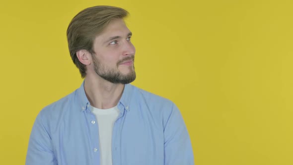 Young Man Pointing on Side on Yellow Background