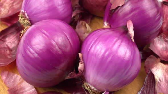 Red onions and dry onion skin are laid out on a wooden board, purple vegetable