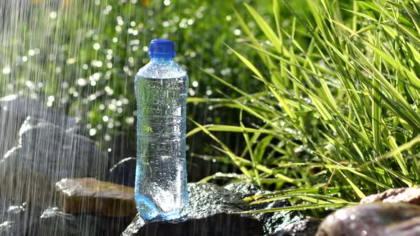 Bottle of water in garden on stones near fountain with water drops