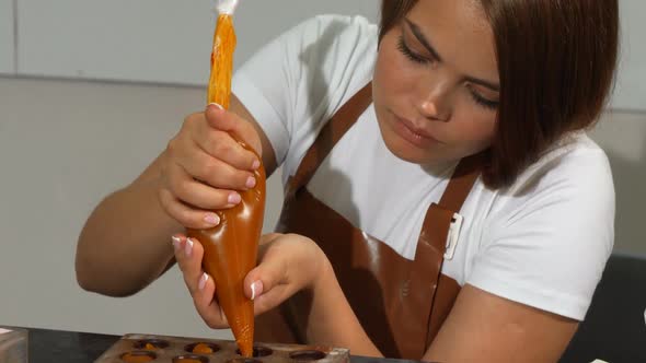 Young Female Chocolatier Adding Filling Into Chocolate Molds