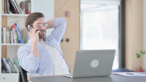 Man in Glasses with Laptop Using Smartphone in Office