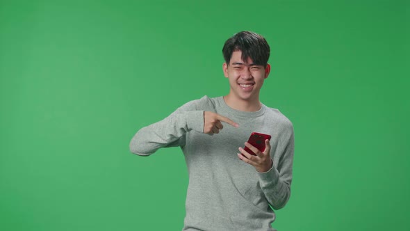 Asian Man Use Mobile Phone And Pointing To Smart Phone Screen While Standing On Green Screen