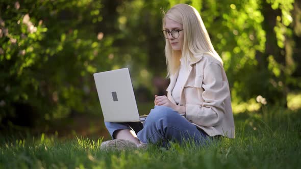 Happy Woman Student Sitting on Green Grass with Laptop in the Park