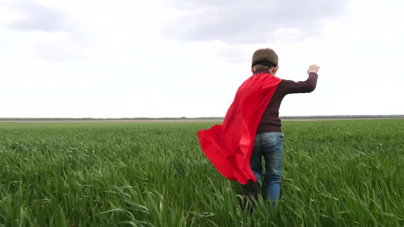 A Child in a Red Raincoat Runs on Green Grass Against a Blue Sky. The Boy Is Playing a Superhero.