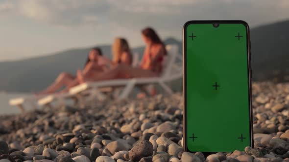 A Phone with a Green Screen and Tracking Points on the Beach Three Multiracial Girls in Swimsuits