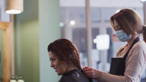 Female hairdresser wearing face mask putting cape on female customer at hair salon