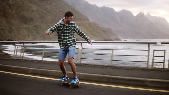 Sport Lifestyle Extreme and People Concept Tall Guy Riding Longboard By the Coastline Road in Cloudy