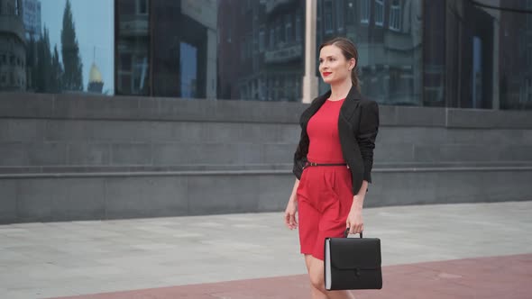 Self-confident Business Woman in a Red Dress Walking Alongside a Business Center, Young Woman