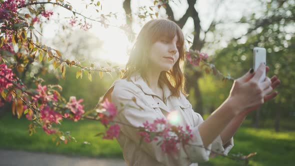 Young Attractive Redhaired Woman Taking Photos of Spring Flowers of Cherry or Sakura Blossoms on