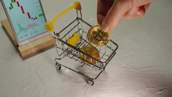 Top view of a man's hand stacking Bitcoin cryptocurrency gold coins in a shopping cart