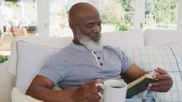 Senior african american man reading book and holding mug of tea