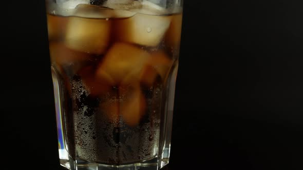 Rotation of a glass with ice cubes and a cola drink on a black background.