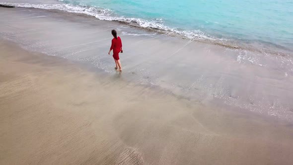 Aerial View of a Girl in a Red Dress Walking on the Beach with Black Sand