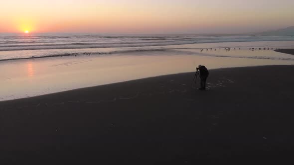 A photographer takes pictures of the Pacific Ocean at sunset (aerial view)