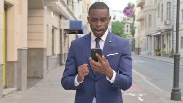 Walking African Businessman Celebrating Success on Smartphone