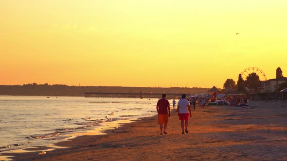 two men are walking on the beach at sunset