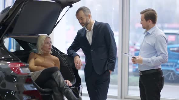 Relaxed Confident Rich Woman Sitting in Car Trunk with Successful Elegant Man Standing and Talking