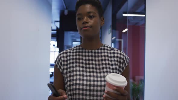 African american businesswoman holding coffee cup walking in office corridor