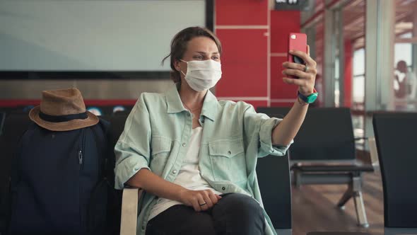 Young Woman in a Protective Mask Sitting at the Airport and Making a Video Call