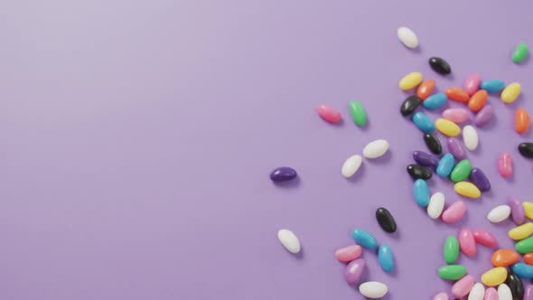 Video of overhead view of multi coloured sweets with copy space over purple background