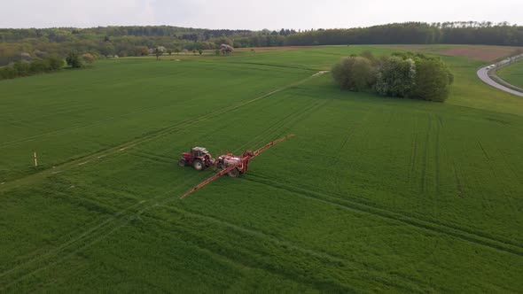 Aerial circular drone footage of a tractor spraying a huge green meadow with water or pesticide with