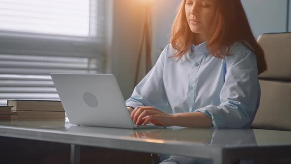 Concentrated red haired nurse with long loose hair types on grey laptop communicating