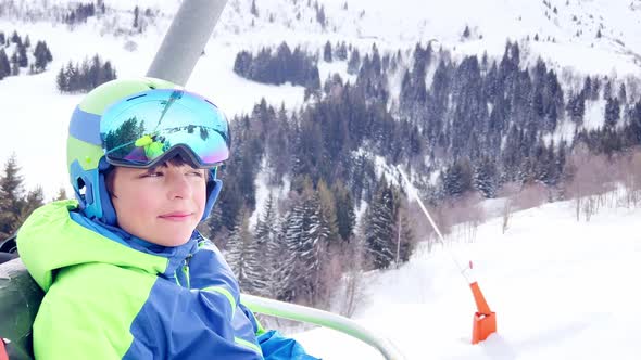 Smiling Boy with Ski Going Up on Chairlift in Mountains