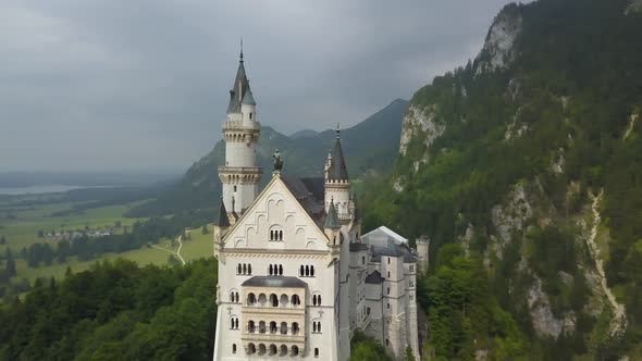 Aerial orbit of picturesque Neuschwanstein Castle on top of a hill surrounded by green dense pine wo