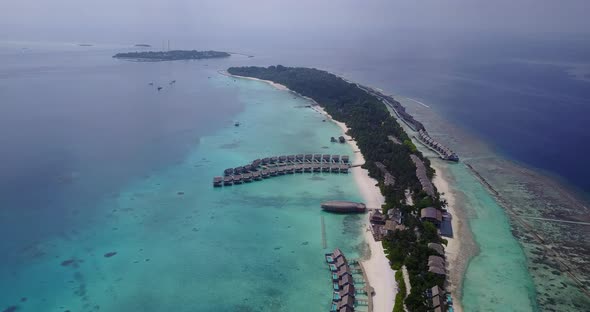 Long tropical island of Maldivian archipelago with lush vegetation and white sandy beach surrounded