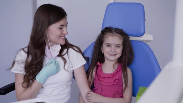 Portrait of Happy Female Dentist and Little Girl Smile at Camera at Dental Chair