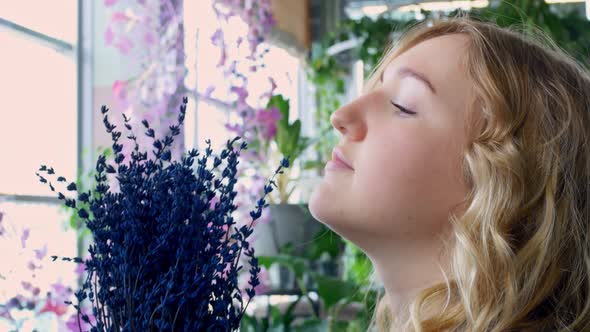 A Pretty Blonde Woman in the Botanical Garden Feels Pleasure Inhaling the Smell of Blue Flowers on