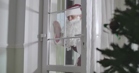 Santa Claus Standing Behind Glass Entrance Door and Waving As Cute Child Running Up and Waving Back