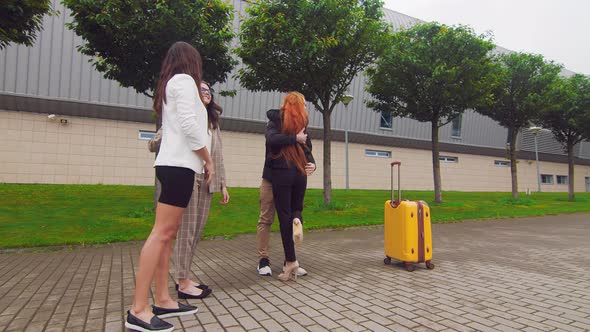 Girl with Red Hair Says Goodbye and Hugs with Friends Going on a Business Trip. Friends Accompany