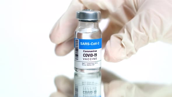 Hand of a Doctor Leaving a Vial of COVID-19 Vaccine on a White Background