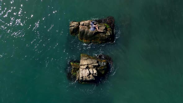 Woman in a Grey Dress and Bathing Suit Lies on a Rock