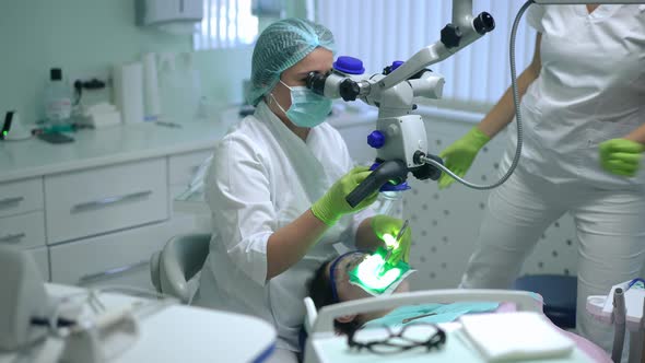 Concentrated Dentist Using Dental Microscope Examining Oral Cavity of Patient As Assistant Sitting