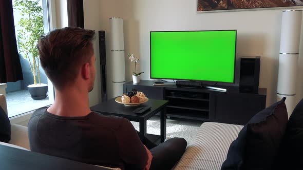 A Man Watches a TV with a Green Screen in a Cozy Living Room