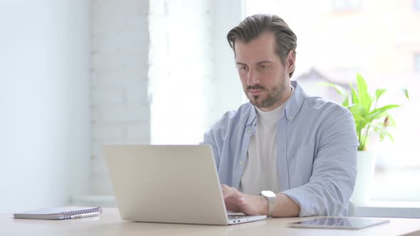 Young Man Looking at Camera While Using Laptop