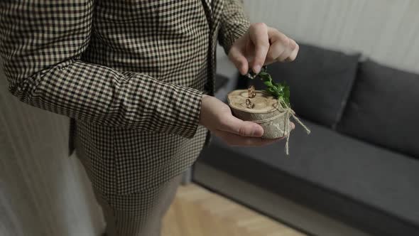 Groom in Brown Jacket Holding Wedding Rings on Wooden Stand on the Palm of Hand. Man Touches Rings